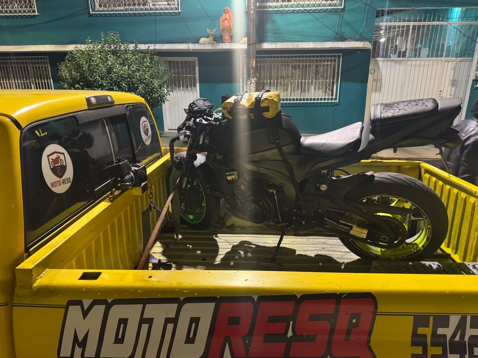 Motocicleta deportiva negra con rines verdes asegurada con correas en la grúa de Moto-ResQ, de noche
